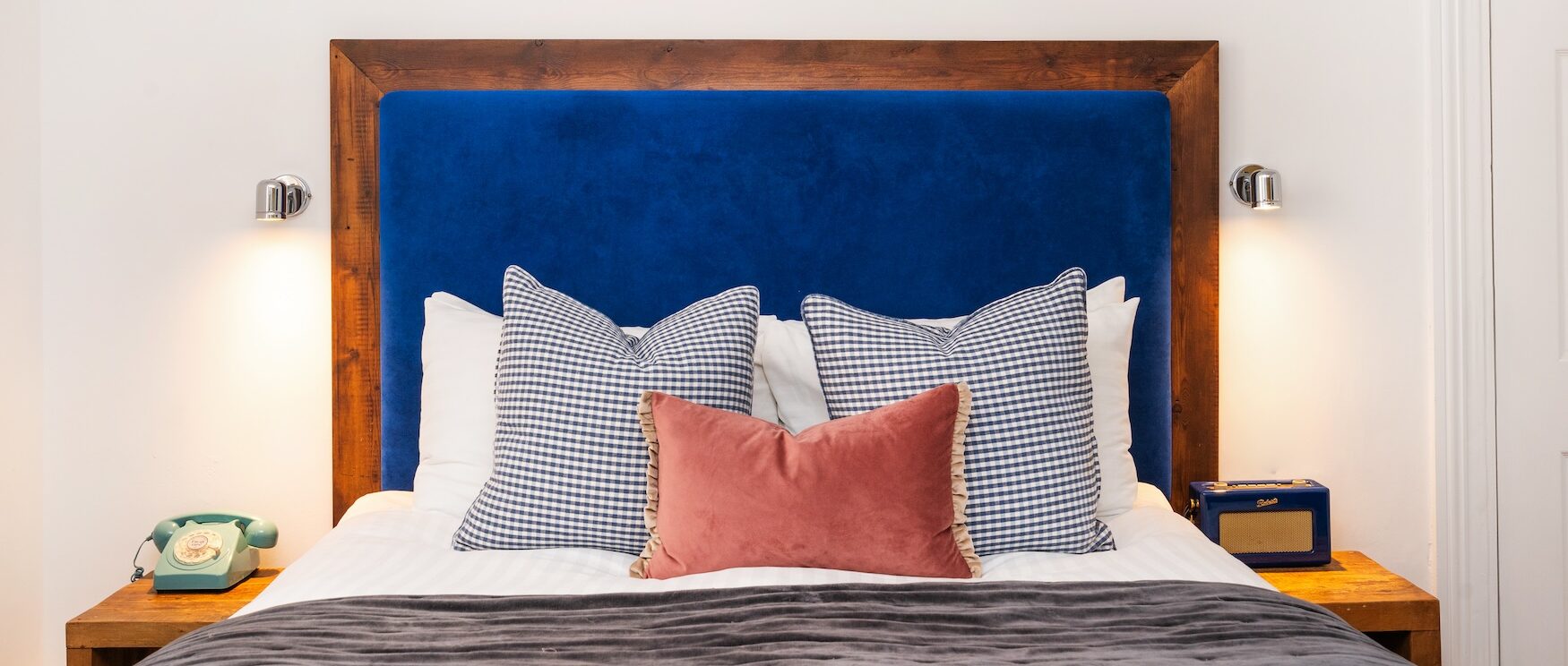 Elegant bedroom at The Berkeley Square Hotel in Bristol, part of The Square Club, featuring a plush blue velvet headboard, designer pillows, and a cosy ambience for a comfortable stay.