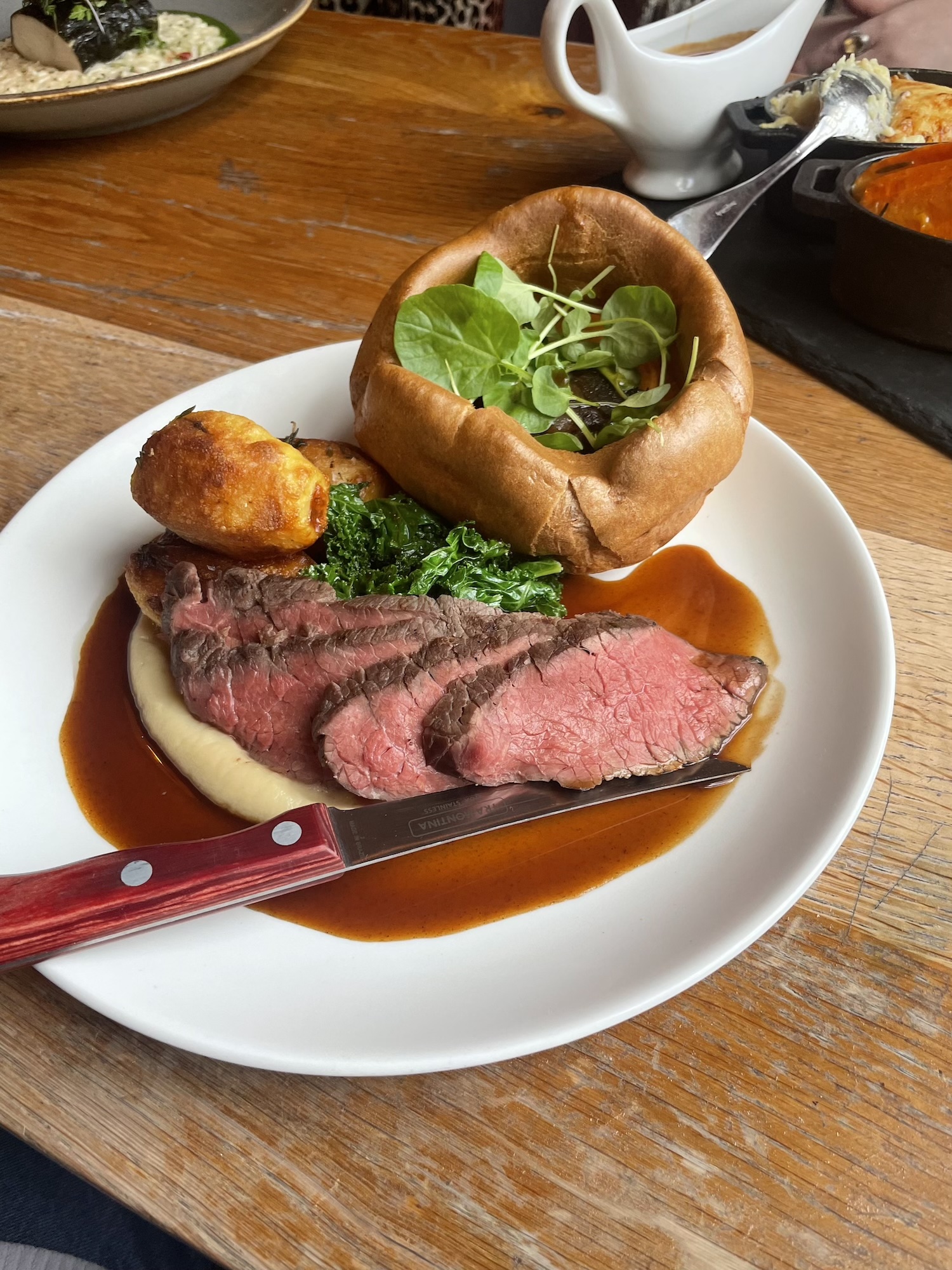 A beautifully presented roast beef dish at The Square Club, showcasing perfectly cooked medium-rare slices of beef, fluffy roast potatoes, creamy mashed potatoes, a golden Yorkshire pudding filled with fresh greens, and a rich red wine gravy. Served with seasonal vegetables as part of the set Sunday lunch menu, this classic British roast is ideal for anyone seeking the best Sunday roast in Clifton. Vegetarian and vegan guests are catered to with equally delicious options, making this venue a favourite for all.