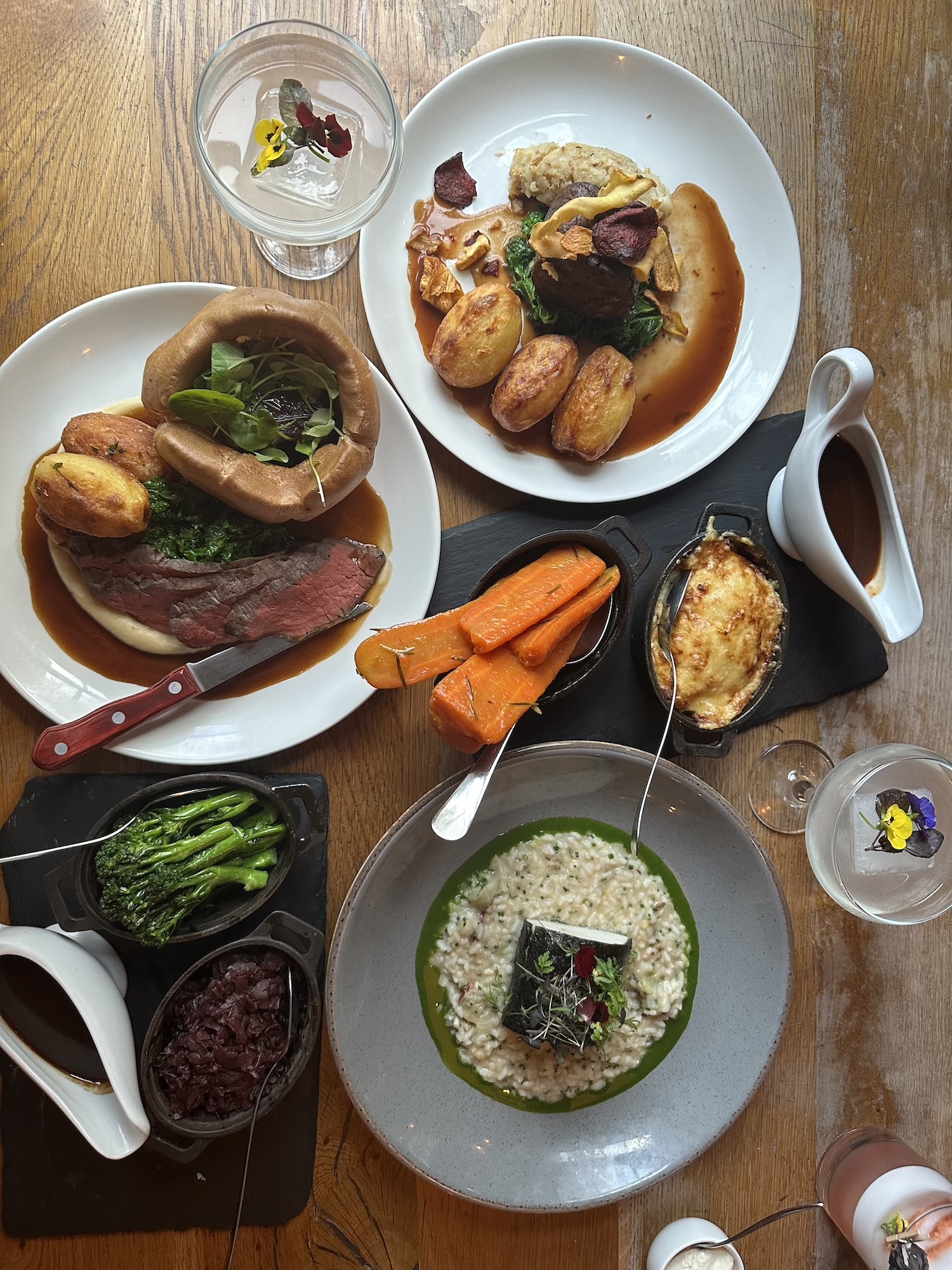 An inviting spread of dishes from The Square Club’s Sunday lunch menu, featuring roast beef with Yorkshire pudding, slow-cooked beef with seasonal vegetables, a vibrant risotto dish with herb garnish, and sides of honey-roasted carrots, sautéed greens, and creamy cauliflower cheese. The Square Club’s menu includes all the traditional trimmings, vegetarian and vegan selections, and desserts, making it a top Sunday roast venue in Clifton for diners seeking the best Sunday lunch in Bristol.