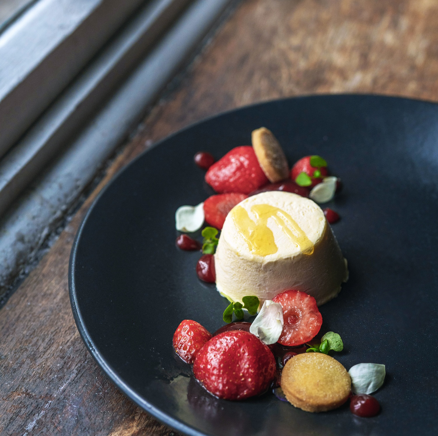 Decadent panna cotta dessert served at The Square Club in Bristol, offering a luxurious private dining experience, beautifully presented with fresh strawberries, biscuit crumbles, and a drizzle of honey.