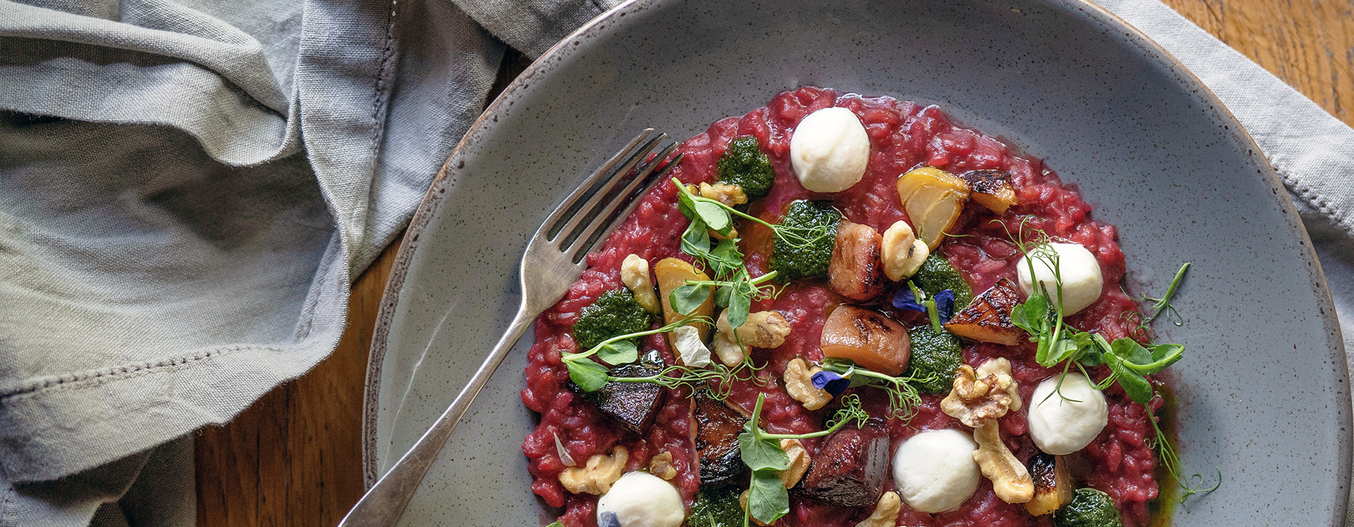 A vibrant beetroot risotto garnished with goat’s cheese, walnuts, and fresh herbs, served in a grey bowl. This comforting and colourful vegetarian dish is a highlight of the menu at The Square Club, a renowned Clifton restaurant in Bristol.