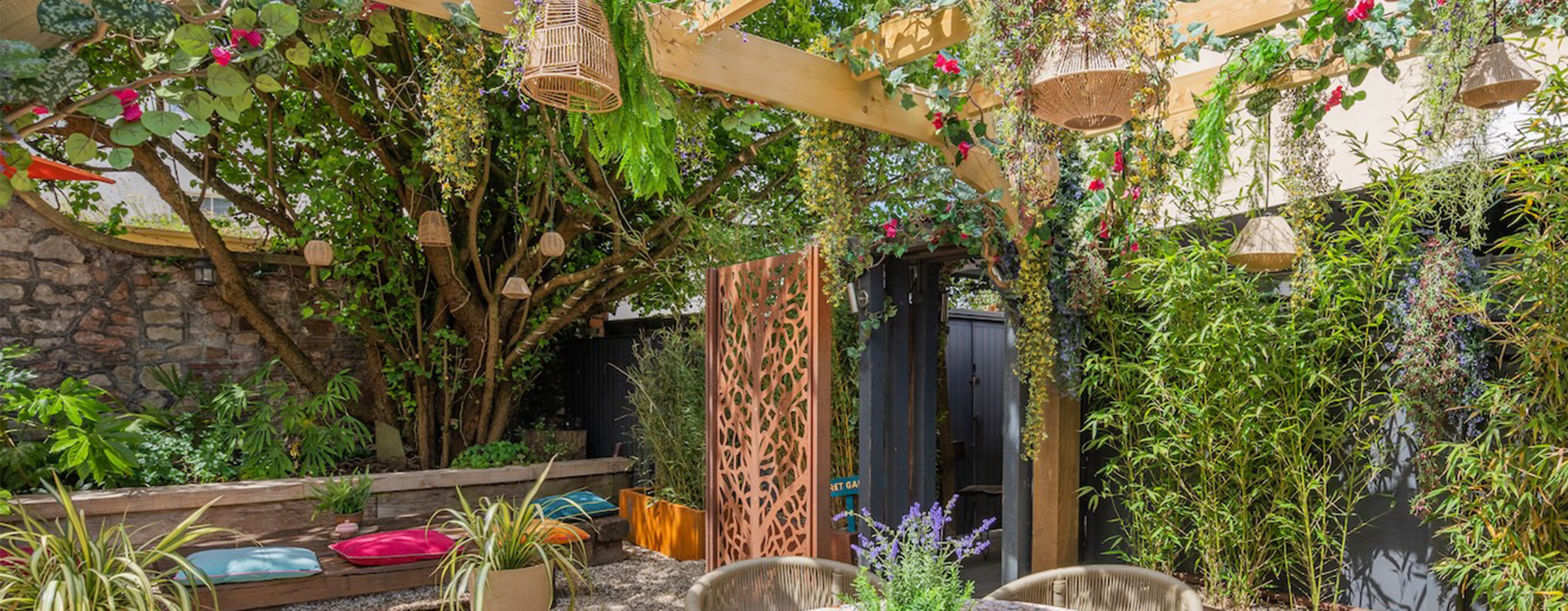 Charming outdoor terrace space at The Square Club, a private members club, featuring a wooden pergola adorned with vibrant hanging plants, comfortable seating, and a natural ambience perfect for relaxation or small gatherings.