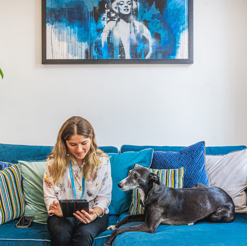 A relaxed moment at Square Works. The award-winning workspace is attached to The Square Club, a private members club in Bristol. A woman reads on a tablet while her dog lounges on a cosy sofa, surrounded by artistic decor and a tranquil atmosphere.