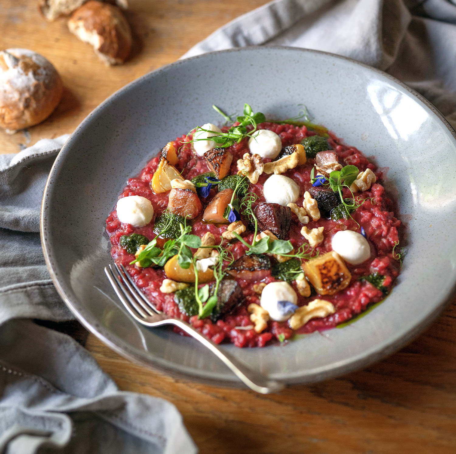 A beautifully plated beetroot risotto served in a grey ceramic bowl, adorned with roasted root vegetables, dollops of creamy goat’s cheese, and garnished with fresh microgreens and walnuts. This dish highlights the seasonal ingredients featured on The Square Club restaurant’s set private dining menu. Ideal for private dining in Clifton or a dinner party venue in Bristol, this vegetarian dish exemplifies the club's commitment to offering exquisite options for all guests, including vegetarians and vegans.