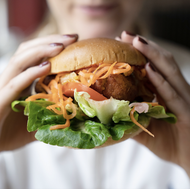 A woman holds a burger at a summer party at The Square Club. The burger contains fresh seasonal ingredients, and is one of many delicious dishes on the award-winning party menus at The Square Club, a party venue in Bristol.